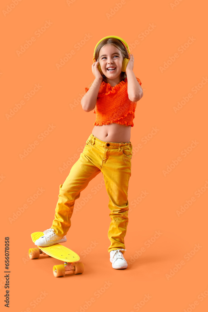 Cute little girl in headphones with skateboard on orange background