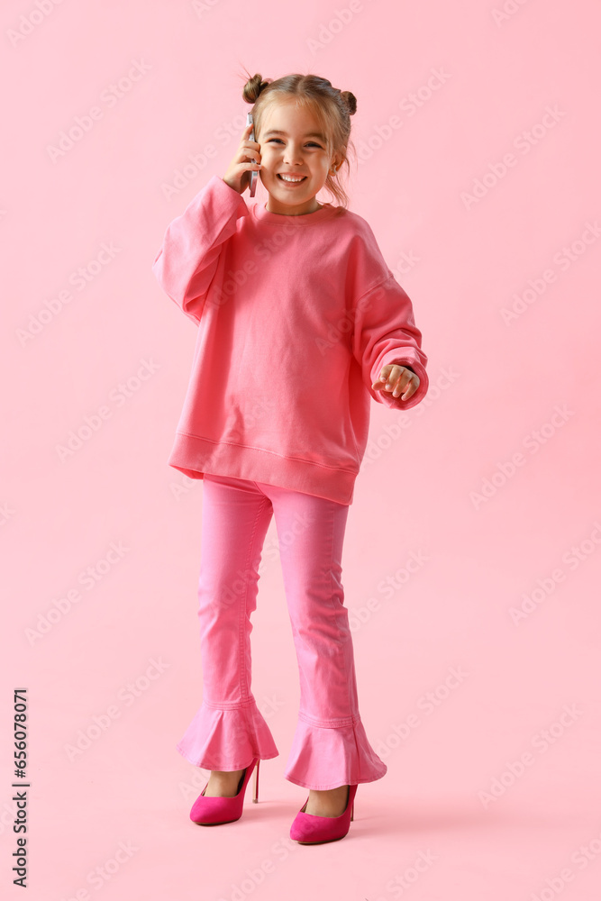 Cute little girl in heels talking by mobile phone on pink background