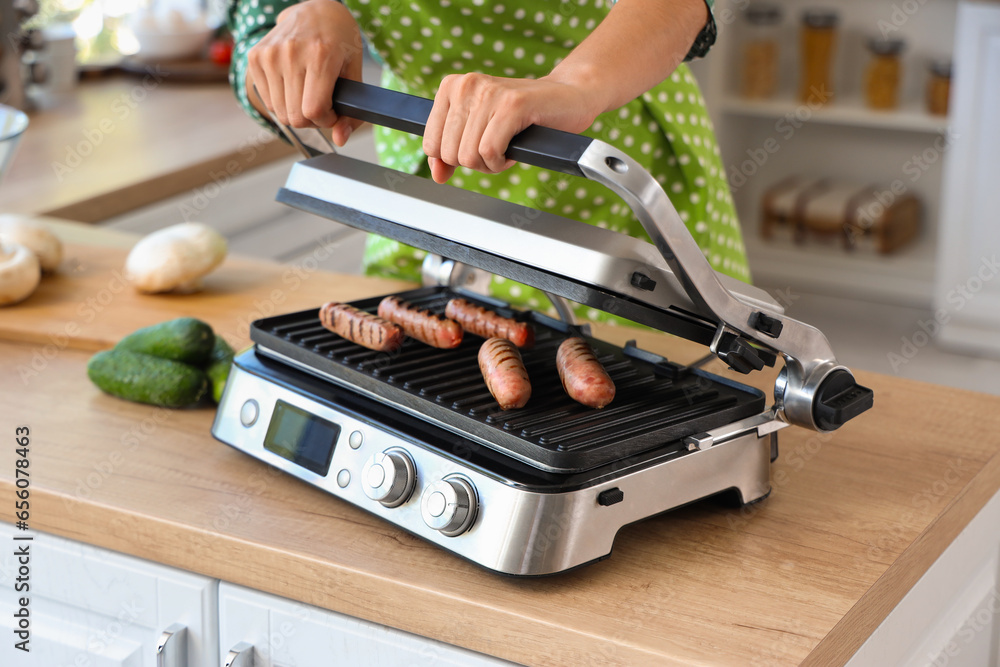 Woman cooking delicious sausages on modern electric grill in kitchen, closeup