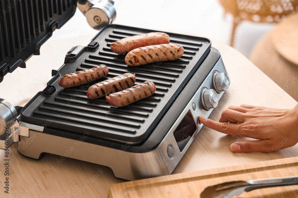 Woman cooking delicious sausages on modern electric grill in kitchen, closeup