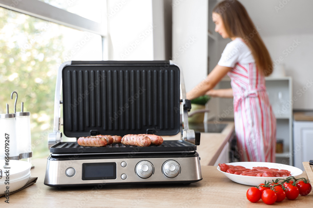 Tasty sausages in modern electric grill with woman on background