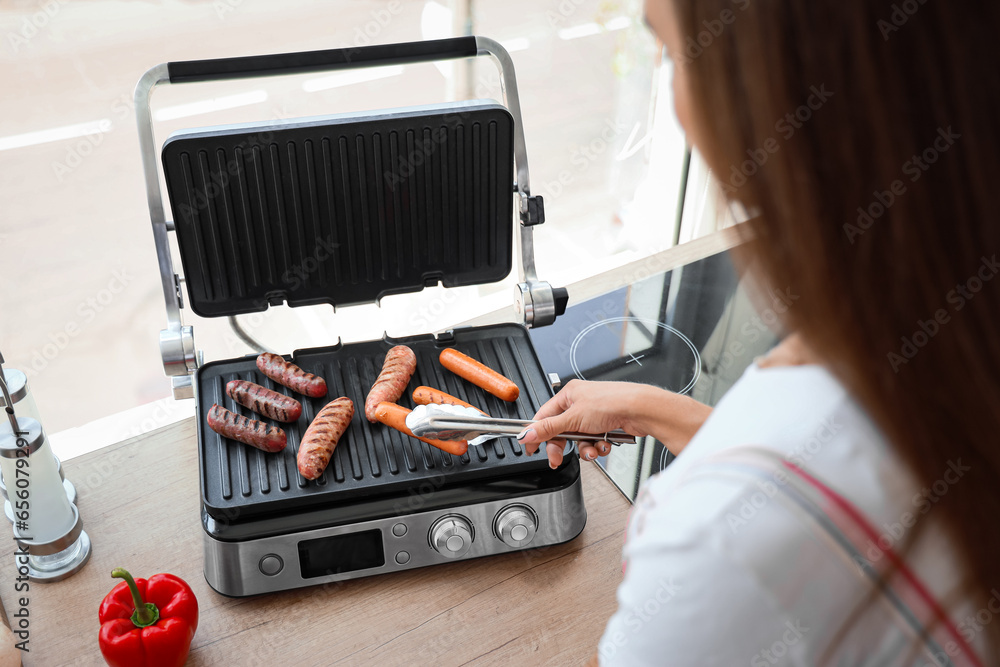 Woman cooking delicious sausages on modern electric grill in kitchen, closeup