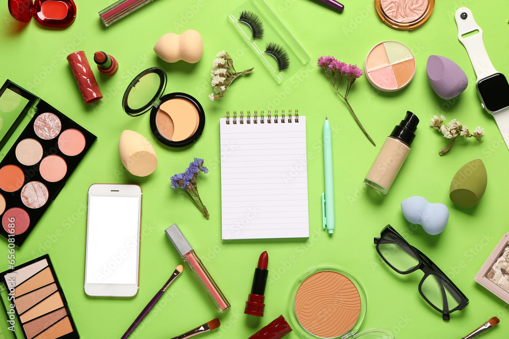 Composition with makeup cosmetics, modern mobile phone, smartwatch, eyeglasses and notebook on green background