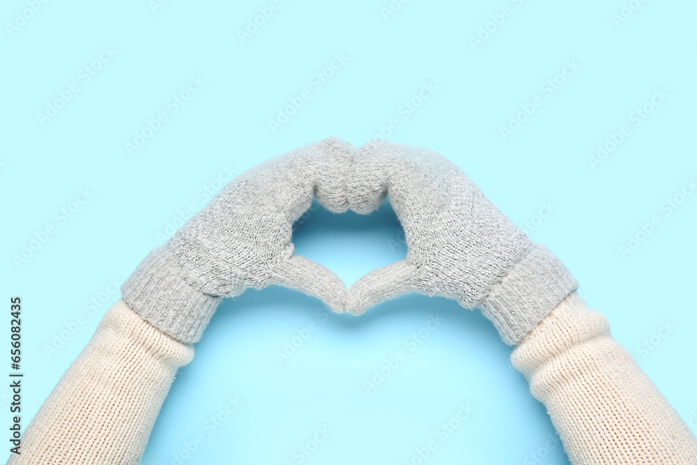 Woman in warm mittens making heart shape with her hands on color background