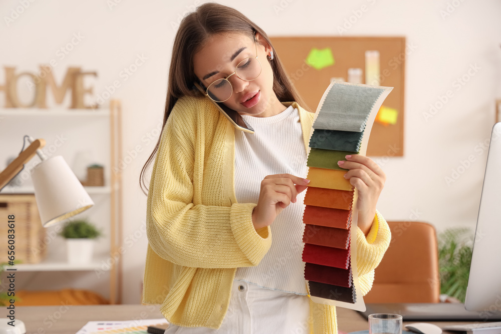 Female interior designer with fabric samples talking by mobile phone in office