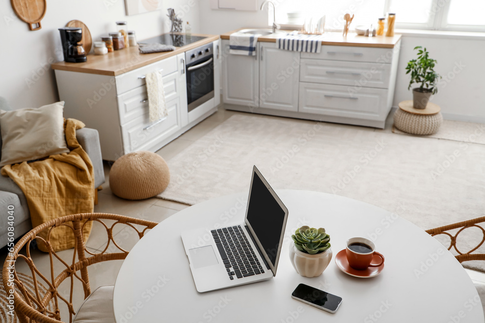 Laptop with mobile phone and coffee cup on dining table in kitchen