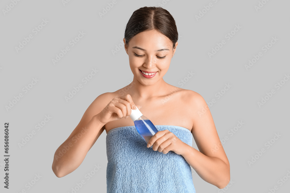 Young Asian woman with bottle of micellar water on light background