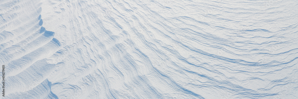 Beautiful winter background with snowy ground. Natural snow texture. Wind sculpted patterns on snow surface. Wide panoramic texture for background and design.