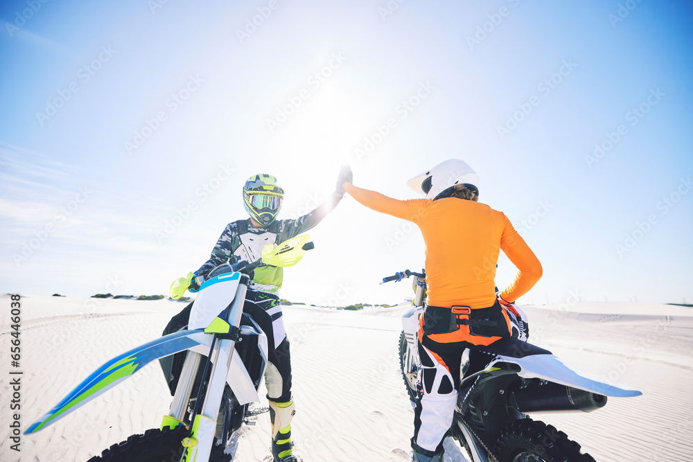 Extreme sport, motorcycle and desert with high five for achievement, skill and teamwork with success. Biker, sunshine and sand with adrenaline, fitness and congratulations for speed with training