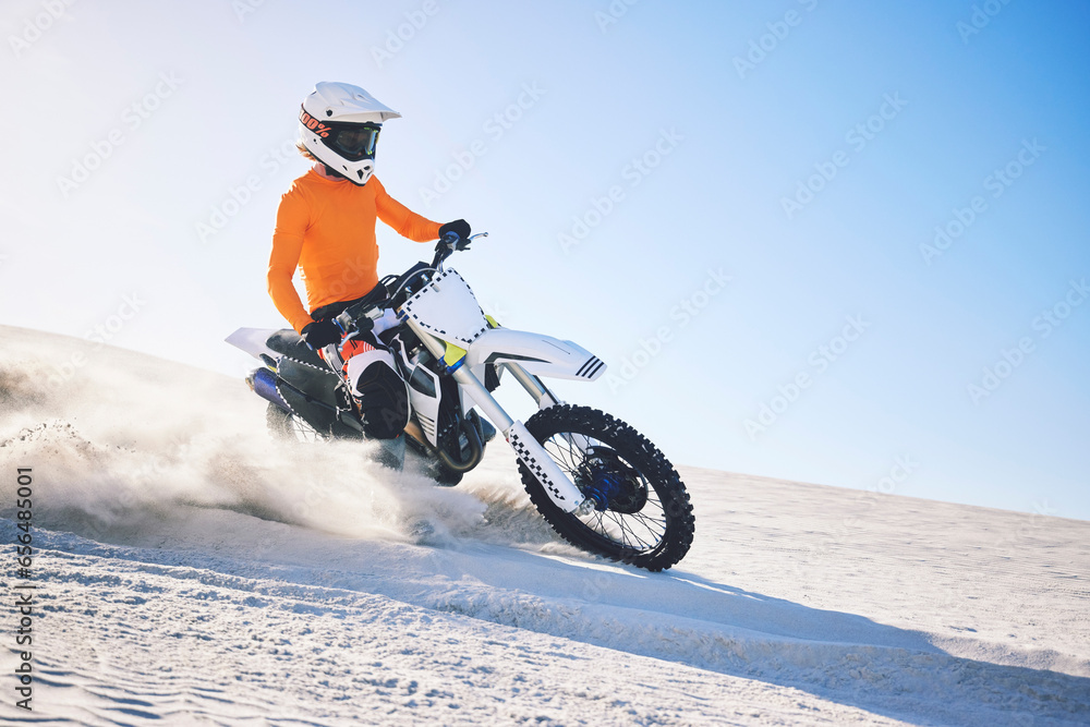 Sport, motorbike and athlete with desert with sand on wheels, pride and skill for adrenaline. Biker, sunshine and dust with blue sky in fun, fitness and achievement in speed, race or dubai vacation