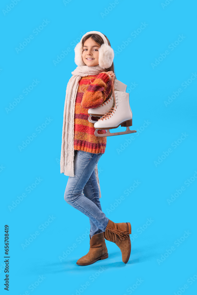 Cute little girl in winter clothes with ice skates on blue background