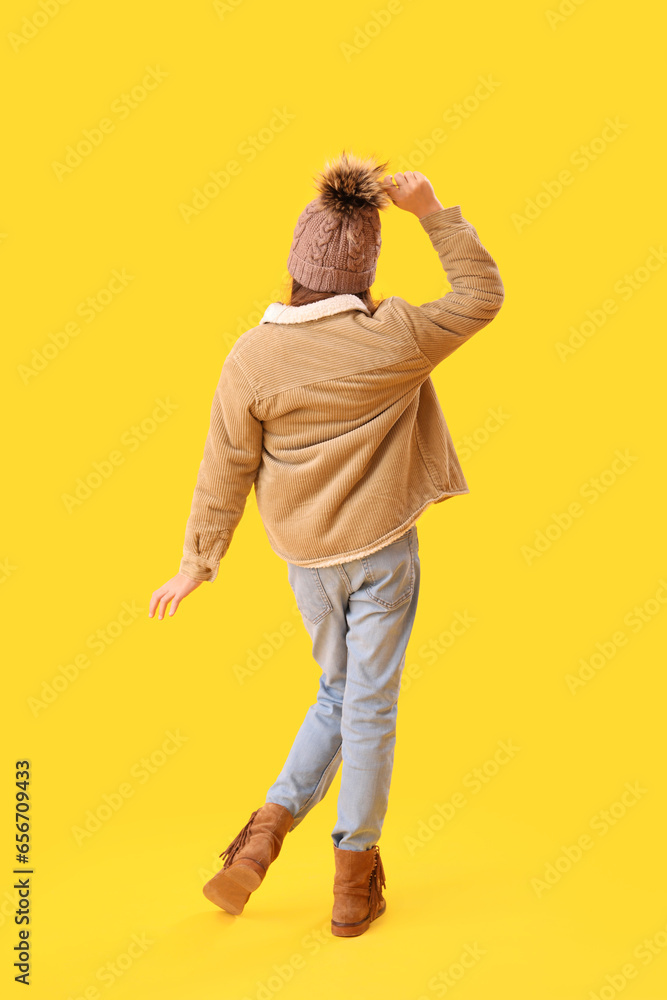 Cute little girl in winter clothes on yellow background, back view