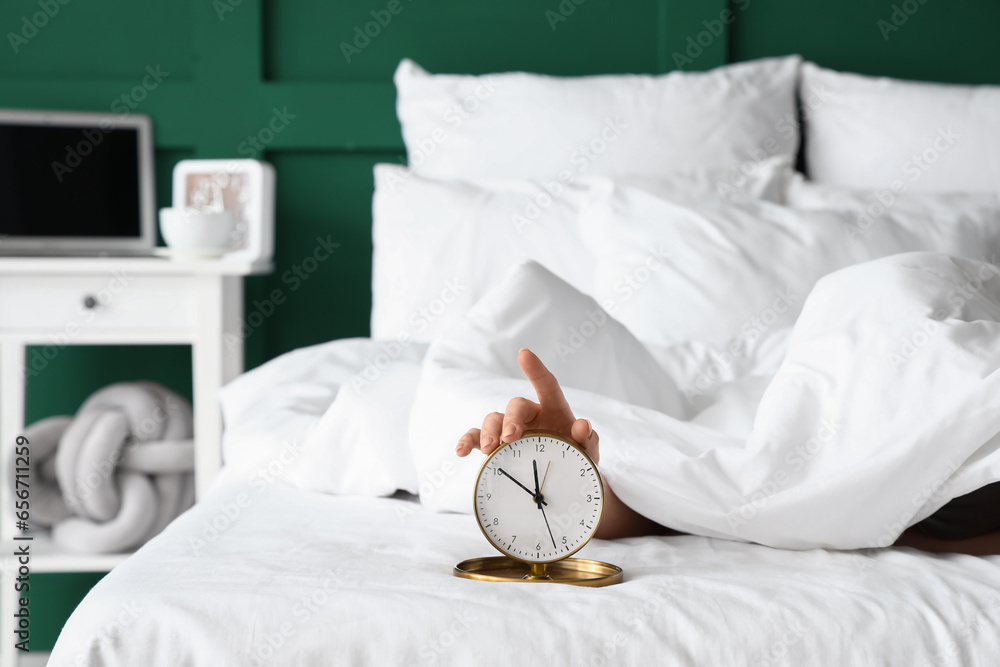 Morning of young woman with alarm clock in bed