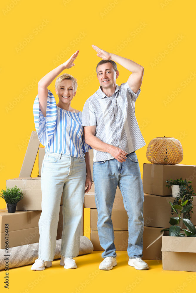 Mature couple with moving boxes on yellow background