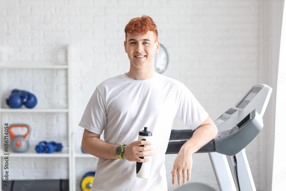 Young redhead man with sports water bottle in gym