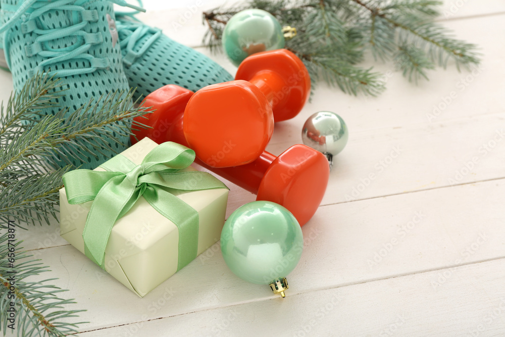 Dumbbells with sneakers, gift and Christmas decor on white wooden background