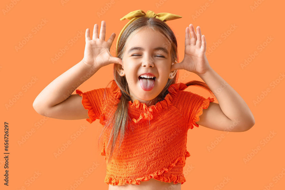 Cute little girl showing tongue on orange background