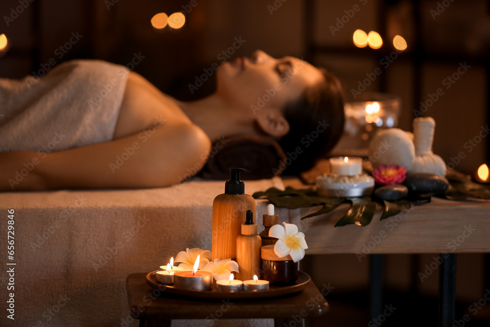 Spa composition with burning candles and plumeria flowers in dark salon, closeup