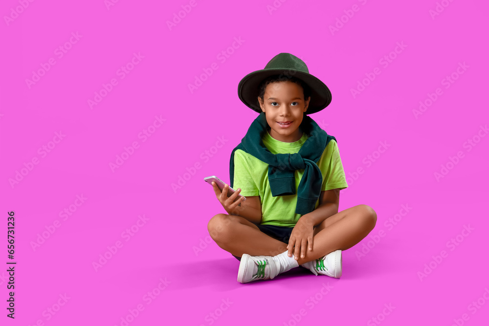 African-American little boy with mobile phone sitting on purple background