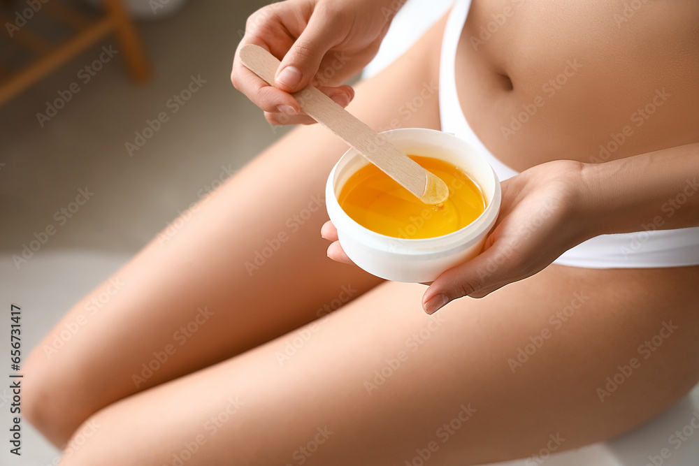 Beautiful young woman with sugaring paste and wooden stick in bathroom, closeup