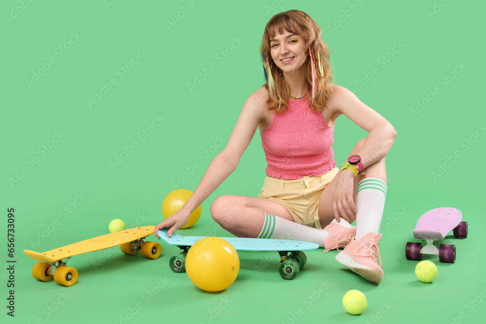 Young woman with skateboards and balls sitting on green background