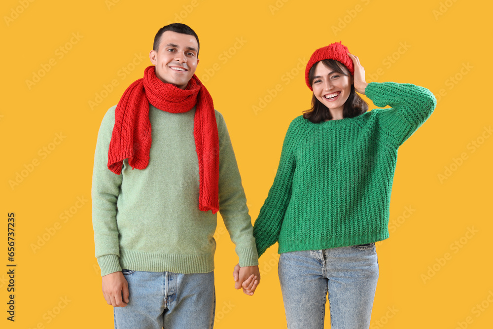 Beautiful young couple in warm clothes on yellow background