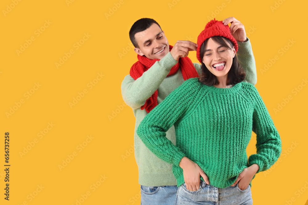 Young couple in warm clothes on yellow background