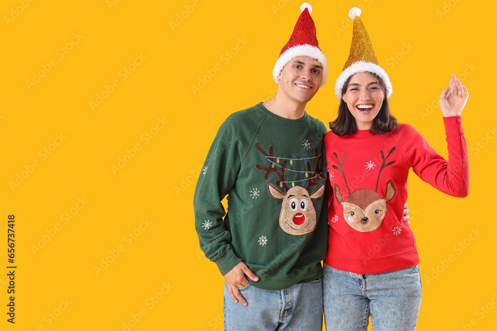 Happy young couple in Christmas clothes on yellow background