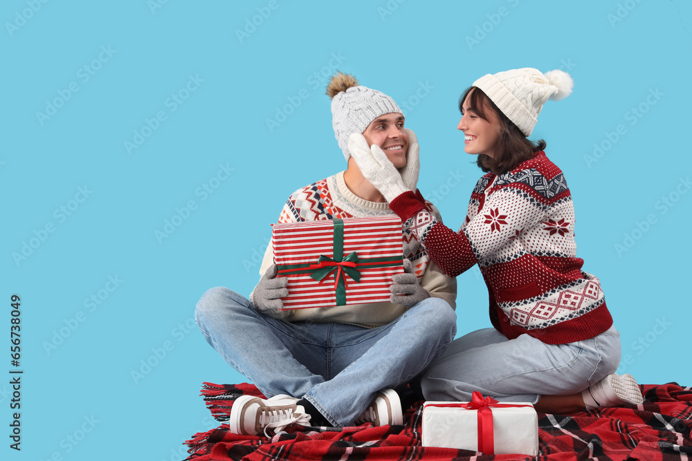 Happy young couple in warm clothes with gift boxes sitting on blue background