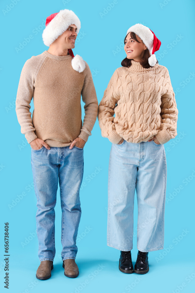 Happy young couple in Santa hats on blue background