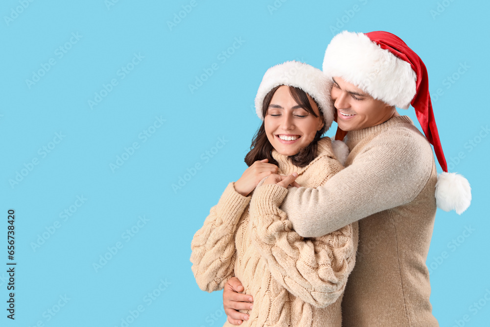 Happy young couple in Santa hats hugging on blue background