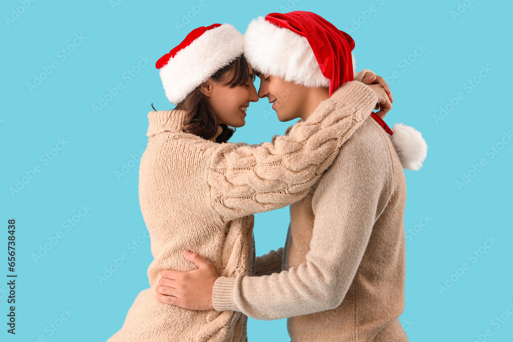 Happy young couple in Santa hats hugging on blue background