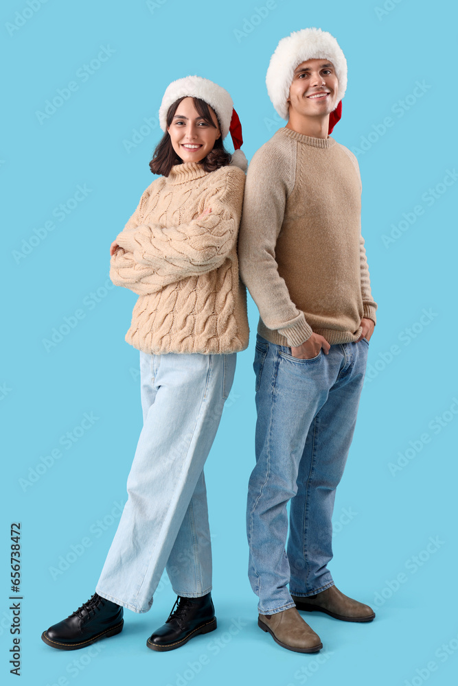 Happy young couple in Santa hats on blue background