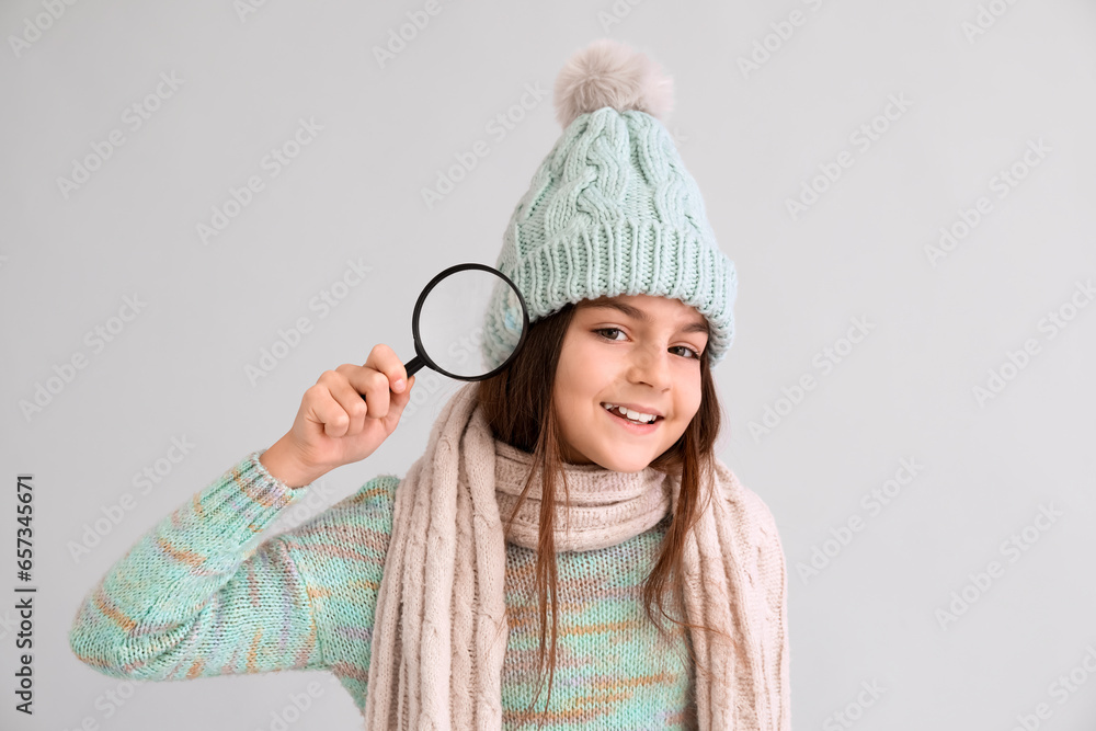 Cute little girl in winter clothes with magnifier on lilac background