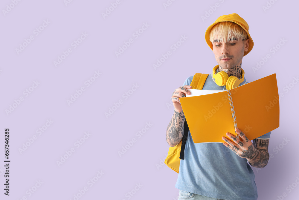 Tattooed male student with notebook on lilac background