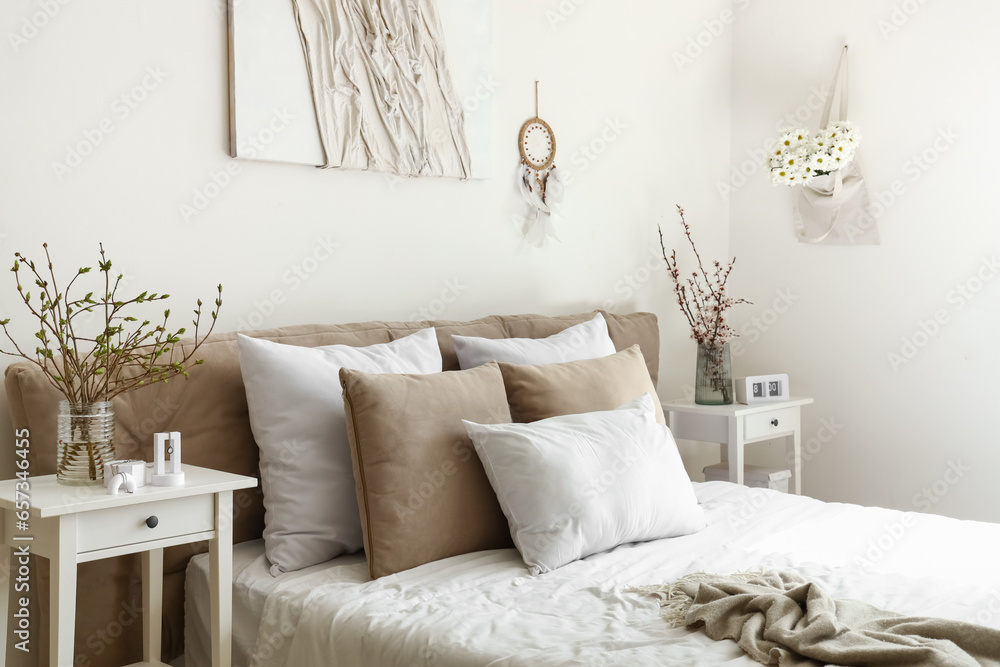 Interior of bright bedroom with blooming tree branches on bedside table