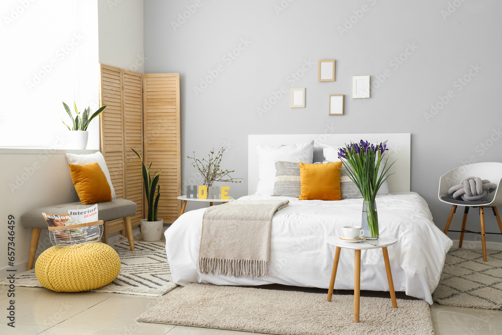 Interior of stylish bedroom with blooming iris flowers on bedside table