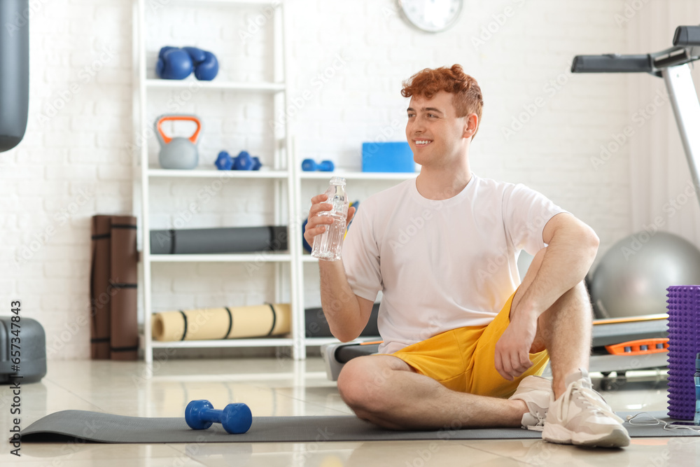 Young redhead man with bottle of water in gym