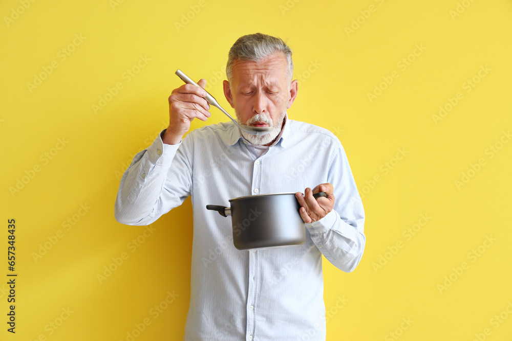 Mature man with ladle and cooking pot on yellow background