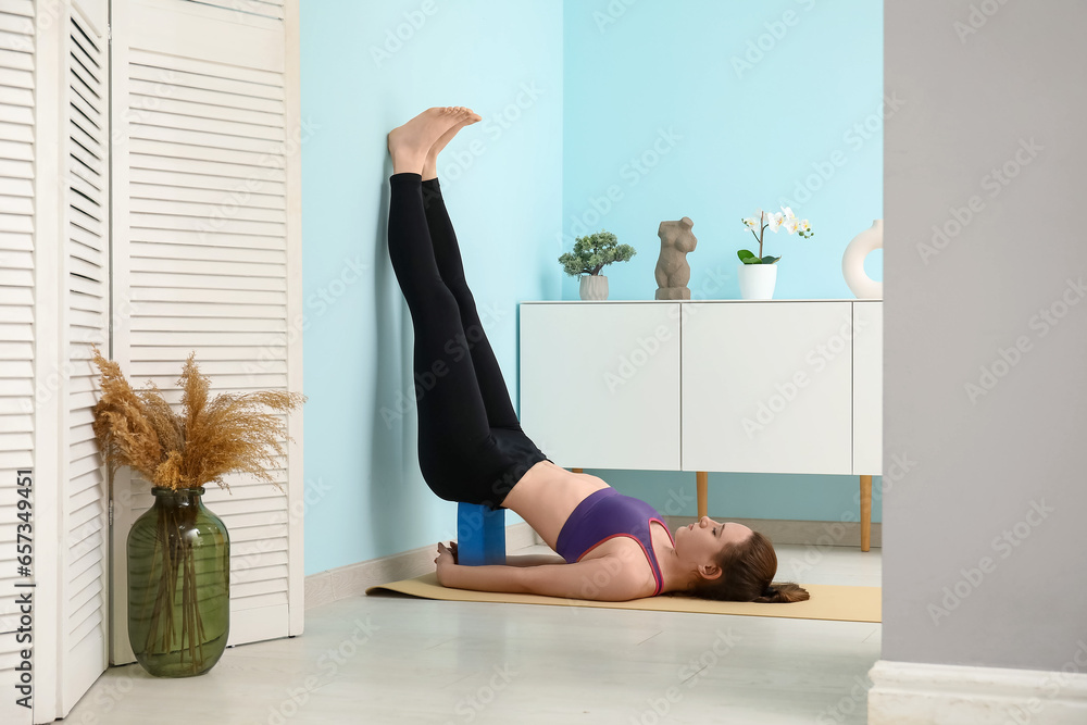 Sporty young woman practicing yoga with block at home