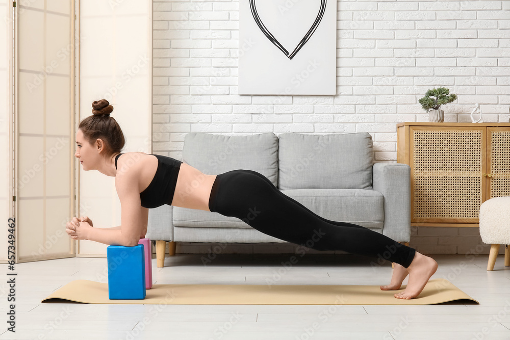 Sporty young woman practicing yoga with blocks at home