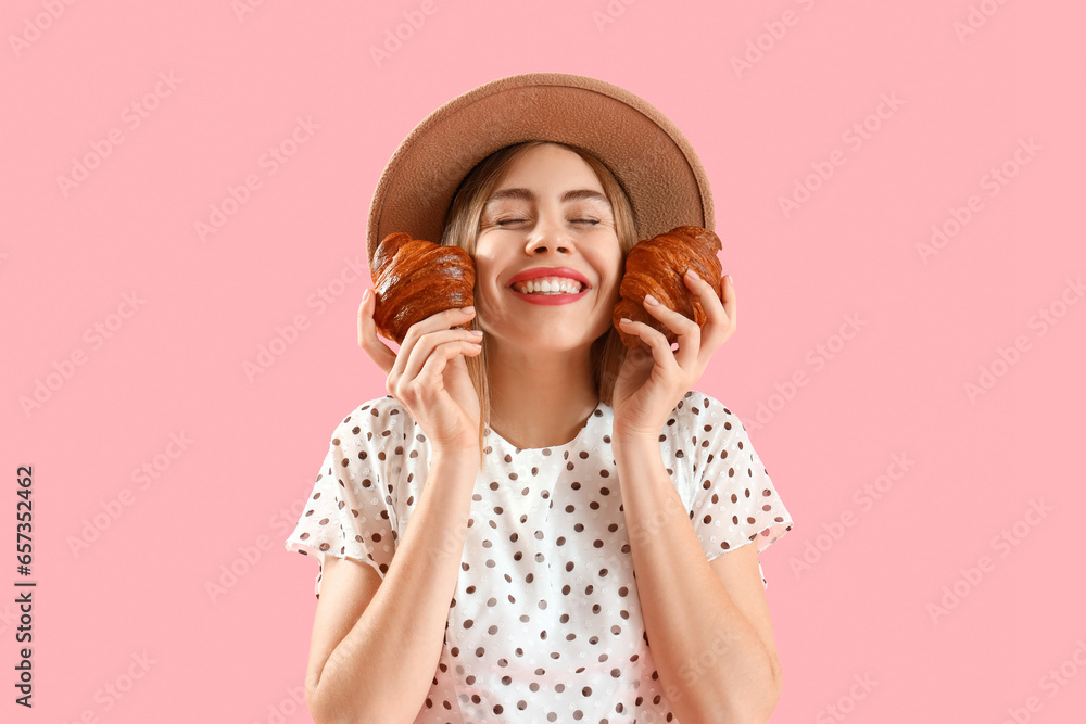 Beautiful happy young woman in wicker hat with tasty croissants on pink background