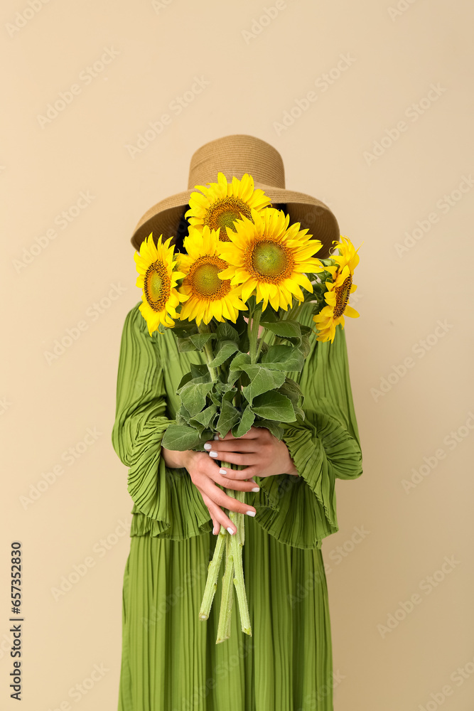 Young woman with beautiful sunflowers on beige background