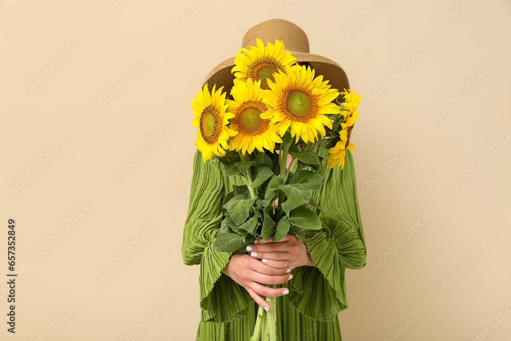 Young woman with beautiful sunflowers on beige background