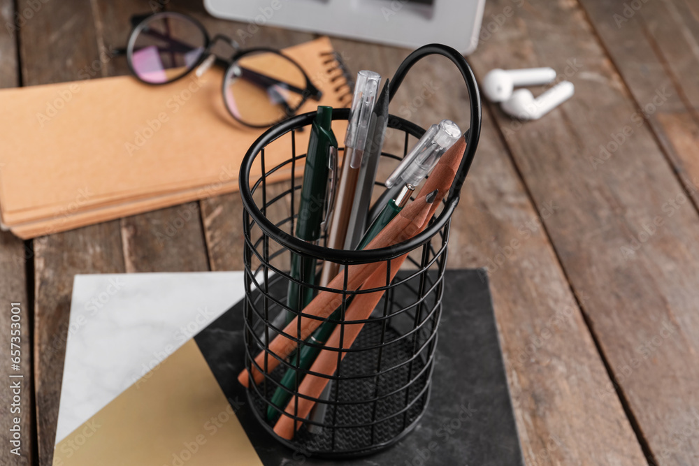 Holder with pens, pencils and notebook on wooden table