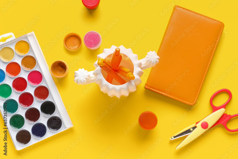 Set of different stationery with paints on yellow background