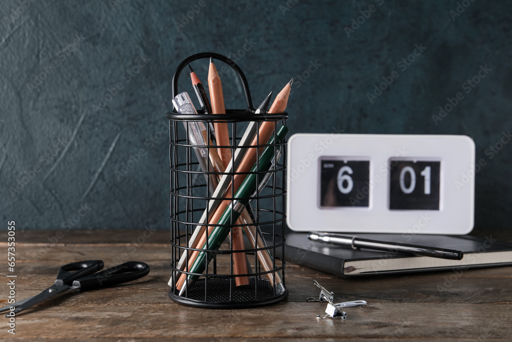 Holder with stationery and alarm clock on wooden table