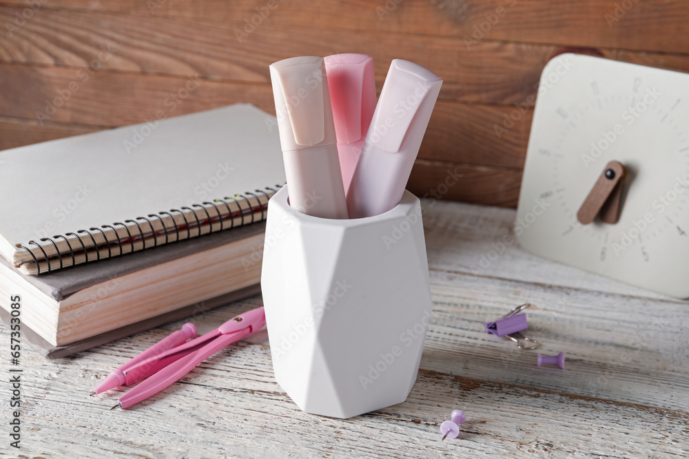 Holder with markers, stationery and clock on light wooden table