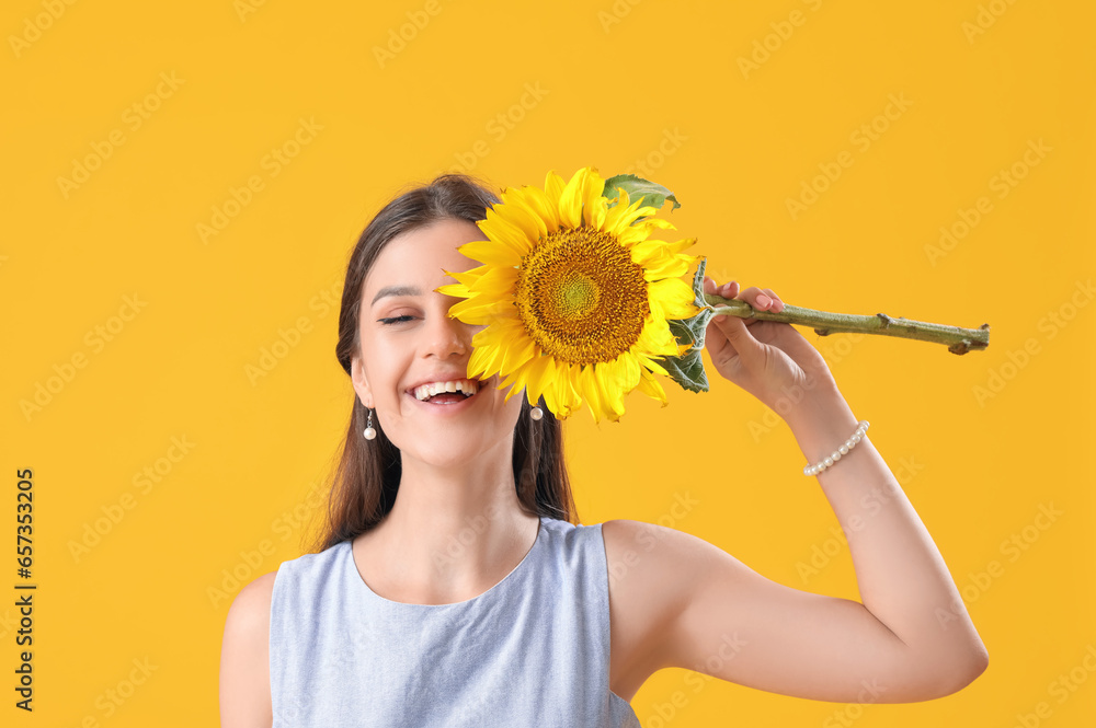 Young happy woman with beautiful sunflower on yellow background