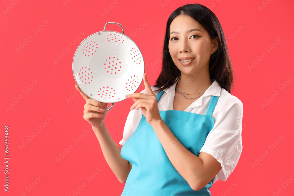 Happy young beautiful Asian woman with colander on red background